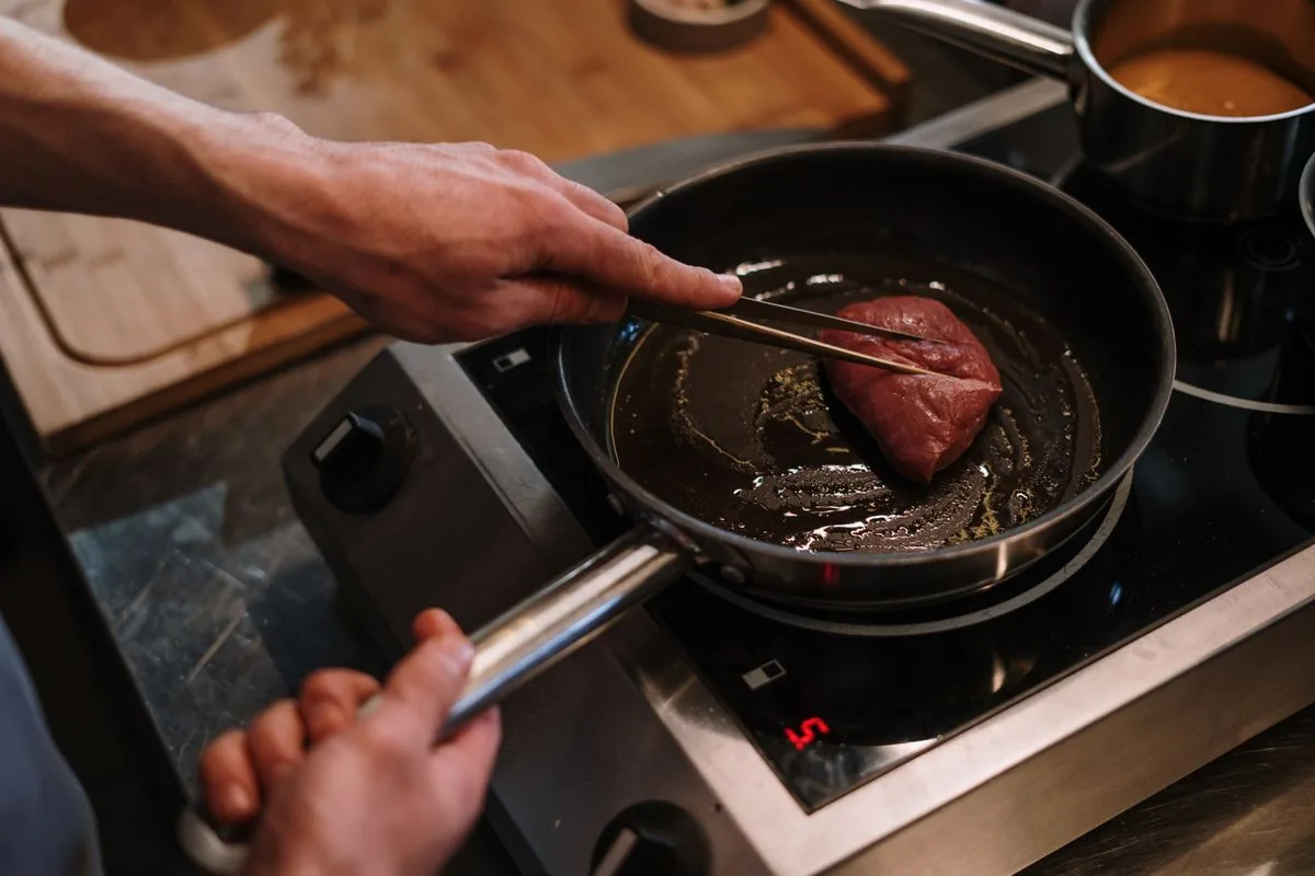 Chef searing steak in a seasoned cast iron pan after reseasoning