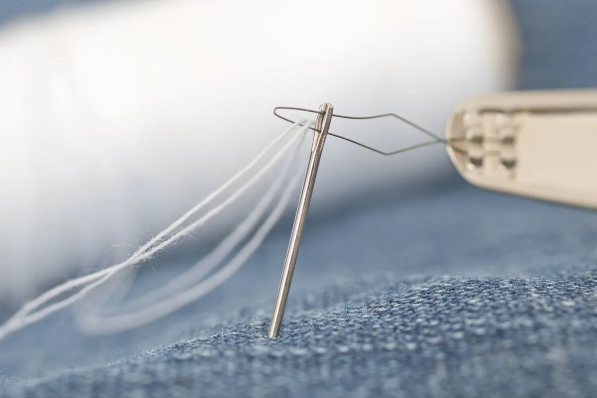 Needle and thread in denim showing shank wrapping for sewn buttons