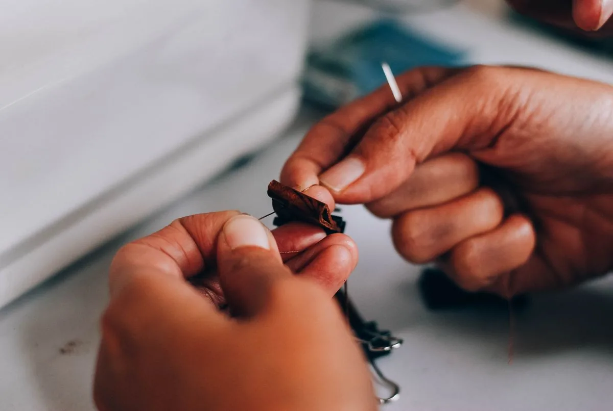 Hands sewing fabric with needle and thread stitching a button
